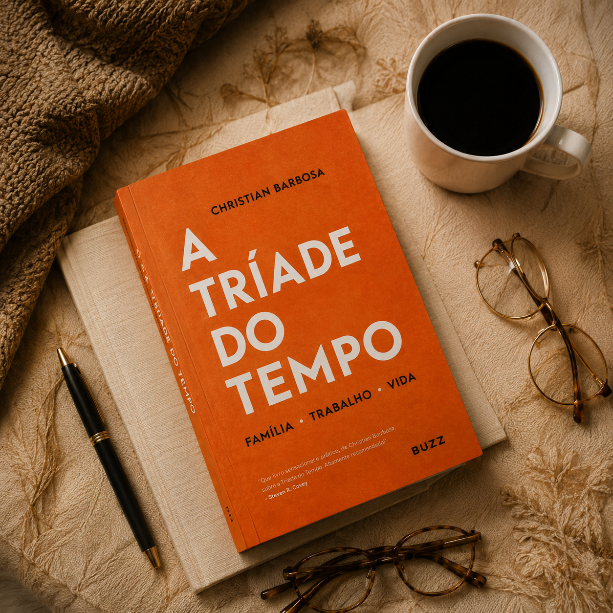 Livro do mês A Tríade do Tempo sobre uma manta, ao lado de café, óculos e caneta